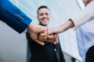 Imagem sobre sucessão empresarial para PMEs mostrando os sucessores de uma pequena empresa dando as mãos em comemoração.